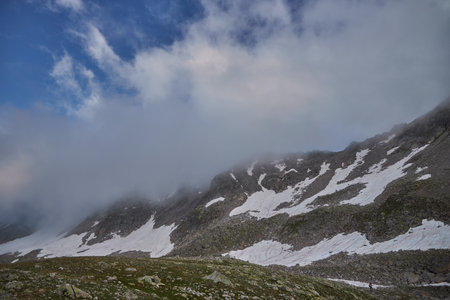 Snow clings to the slopes of a rugged mountain range, peeking through wisps of mist under an...