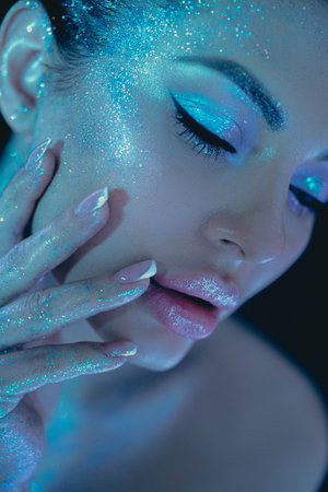 Woman cosmic themed glitter beauty makeup, highlighting eyes and cheeks under blue lighting