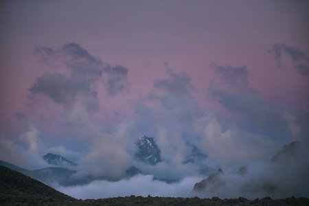 Snow covered mountain peak rises above the clouds under a twilight sky