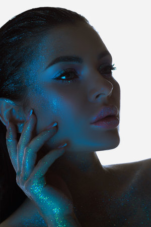 Close-up of a serene woman, her skin sparkling under a soft blue light, gazing into the distanceの写真素材