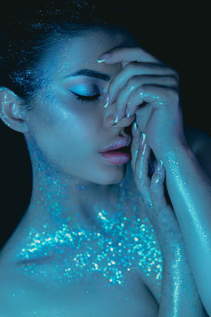 Beauty woman cosmetic makeup, glitter adorning her skin, under dim blue lightingの写真素材