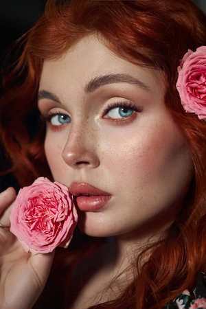 Beauty young redhead woman gazes forward amidst delicately suspended pink roses against a dark backgroundの写真素材