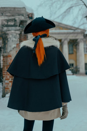 Woman standing in the snow while wearing a black coat and cape, showcasing winter scenery