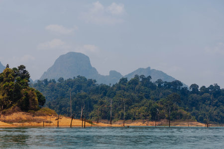 A calm lake reflects the surrounding landscape, featuring vibrant greenery and a distant mountain...