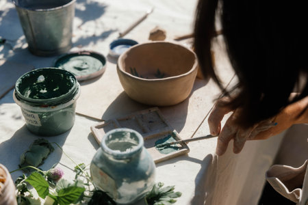 An artisan applies green paint to a canvas using a brush, surrounded by various natural materials...
