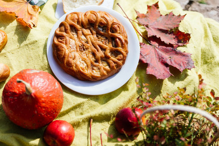 A delightful autumn picnic is set up with a round pastry centerpiece, surrounded by vibrant fall...