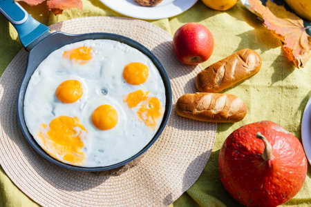 Gathered on a colorful picnic blanket, a delicious breakfast includes fried eggs with bright yolks,...