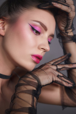 woman poses gracefully, highlighting her vibrant pink eye makeup and bold lip color. intricately designed black lace gloves add a chic touch to her sophisticated look.の写真素材