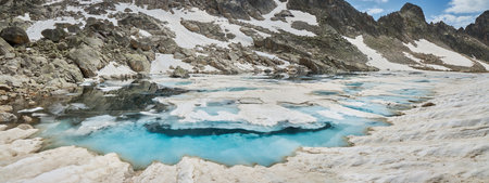 Under a bright blue sky, a glacial lake reflects shades of turquoise among rocky terrain.の写真素材