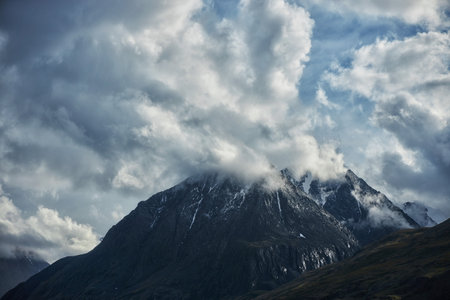 Snow-capped mountain rises dramatically above the landscape, enveloped in clouds. sky is painted...