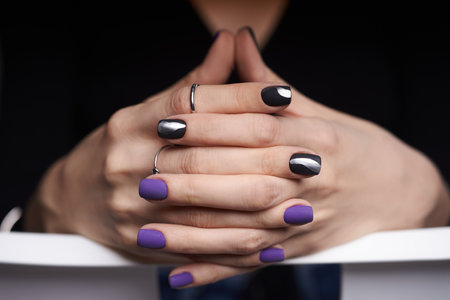 Hands with stylish nails exhibit a combination of matte purple and glossy black colors, enhanced by silver accents. Nails are neatly filed with careful attention to detail and design.の写真素材