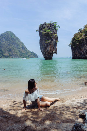 Enjoying a tranquil moment on the sandy shore while overlooking unique rock formations rising from the sea on a bright day in Thailandの写真素材