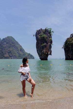 woman stands at the shoreline, gazing out at striking rock formations rising from turquoise waters.の写真素材