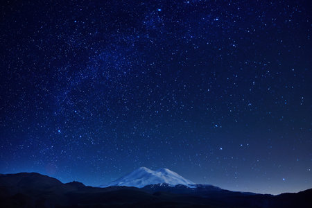 breathtaking view of a mountain with a snow-covered summit set against a clear night sky filled with vibrant stars and a rich backdrop of deep blue hues, creating a serene atmosphere.の写真素材