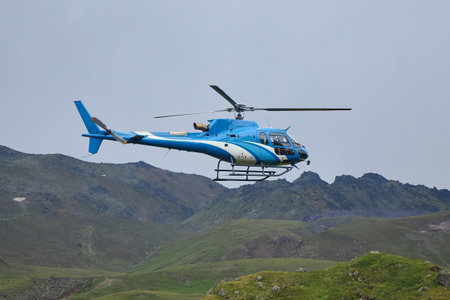 blue helicopter soars above the rugged mountain terrain, navigating through the cloudy sky....