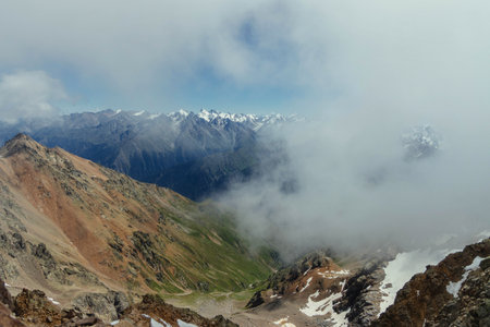 Clouds drift through the rugged mountain landscape, revealing stunning peaks and deep valleys under blue sky. captivating view showcases natures majesty and beauty during daylight hours.の写真素材