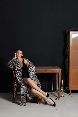 model reclines gracefully on a chair wearing a leopard print coat and a black outfit.の写真素材