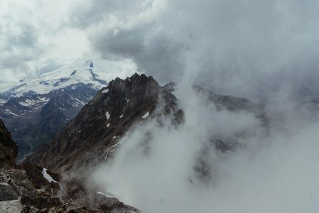 Rugged mountain peaks rise dramatically into the sky, partially hidden by swirling clouds and mist....
