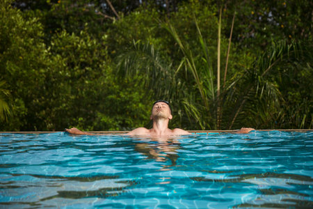 man enjoys a peaceful moment while floating in a pristine infinity pool, soaking in the warmth of the sun and surrounded by vibrant greenery.の写真素材