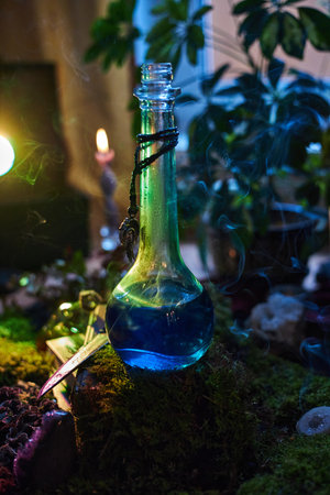 captivating glass bottle filled with blue liquid sits on moss. Soft candlelight and greenery create an enchanting atmosphere during the evening hours.の写真素材