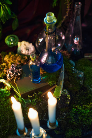 table is adorned with various glass bottles filled with blue liquid, surrounded by candles and natural elements. scene captures a mystical, enchanting atmosphere in the dim light.の写真素材