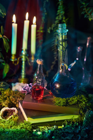 Colorful glass bottles filled with potions rest on a stack of books surrounded by candles and lush greenery. ambiance is magical and inviting, perfect for a fantasy scene.の写真素材