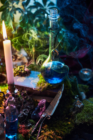 glass bottle filled with a vibrant blue potion sits on a wooden surface surrounded by moss, candles,...