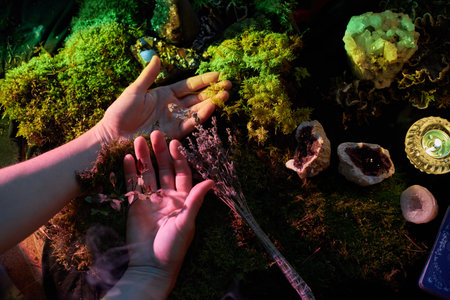 Two hands extend, cupping dried herbs and holding crystals above a rich green moss backdrop. Soft light highlights various natural elements on the altar, creating an enchanting atmosphere.の写真素材