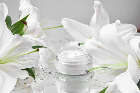 small cream jar sits on a shiny surface, surrounded by fresh white lilies. setting offers a calming and elegant vibe, perfect for skincare products or beauty rituals.の写真素材