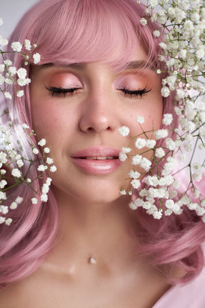 woman with soft pink hair enjoys a peaceful moment surrounded by delicate white flowers. Her expression reflects tranquility and joy at a floral celebration in a bright setting.の写真素材