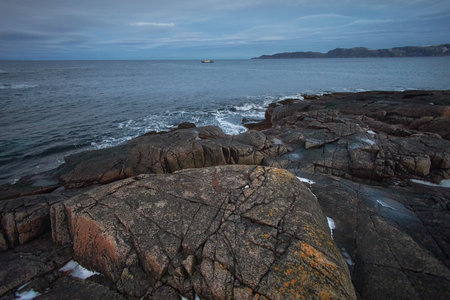 Visitors walk along the rugged shore of Teriberka, Russia as a small boat sails in the distance...