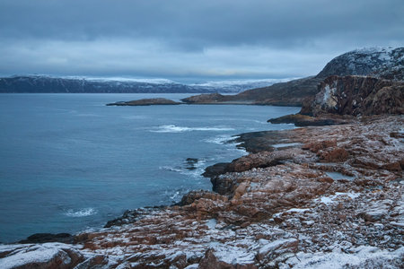 Visitors experience the rugged coastline of Teriberka in Russia, surrounded by snow and water. The landscape showcases rocky formations and distant hills.の写真素材