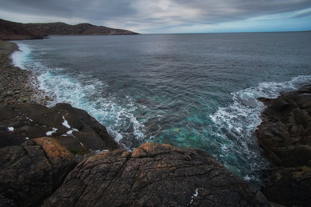 Waves hit the rocky shoreline in Teriberka, Russia while the sky is covered with clouds and the water reflects various shades from the cold season.の写真素材