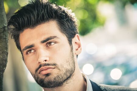 Handsome man, close portrait of young man with stubble beard. Near to a tree.の写真素材