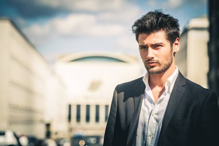 Man in suit and white shirt looking. With fashionable hair and beard. Outdoors on the street in the...