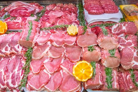 Meat department in butchery inside a mall. Various types of meat displayed in an orderly and creative way. Shelves of a food supermarket. Orange and vegetables for decoration and topping.の写真素材