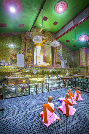 Mandalay, Aungmyaythazan, Myanmar. July 24, 2019: Some Buddhist nuns in prayer kneeling in front of the Buddha statue in the Su Taung Pyae Pagoda temple.のeditorial素材