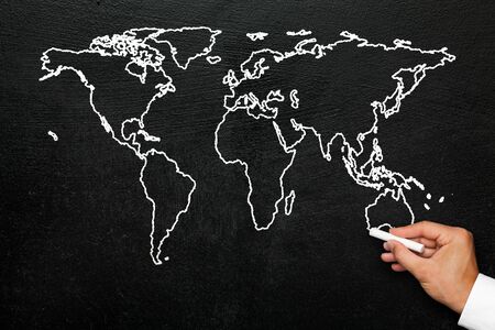 World map on blackboard. A hand draws a stylized globe map of the world with all continents with...
