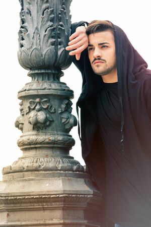 Gorgeous young man leaning against a old streetlight lamppost. Hansome and young man with hoodie.