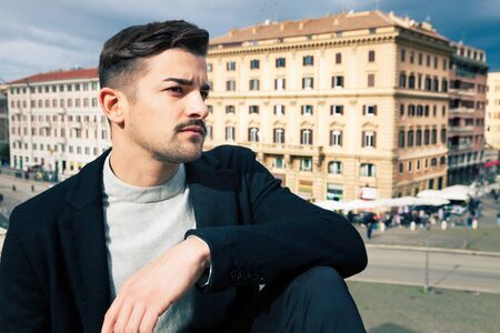 Young and handsome man portrait. In the street in the city during the day. Buildings behind him.の写真素材