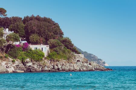 Italian maritime coast of the Island of Elba with rocky ridge and perched house. Sea, trees and rocks in Italy in the city of Procchio.の写真素材