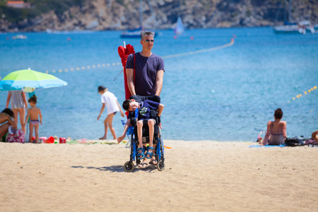 Elba Island, Italy. June 25, 2016: Young disabled boy in the wheelchair with a companion on the...