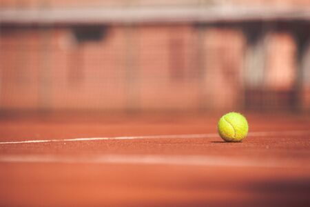 Yellow tennis ball on a clay court. Playing tennis outdoors. The ball is illuminated by the sun. Selective focus.の写真素材
