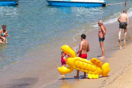 Procchio, Italy. June 26, 2016: Some people are on the shore of the sea during the summer vacation. A man is holding an inflatable mattress in the shape of lobster. Elba island, Tuscany in Italy.のeditorial素材