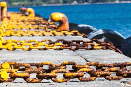 Harbor, sea holidays. Chains. Summer season, yellow chains mooring in a port. Background with infinite chains, tires, blue sea.の写真素材