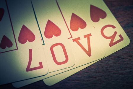 Love, poker playing cards with heart symbol that form the written love. On a wooden shelf. Idea for greeting card for Valentine's Day or other occasion.の写真素材