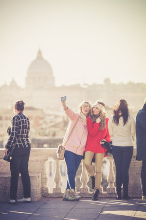 Rome, Italy. January 10, 2016: Tourists and people on the Pincio terrace in Rome in Italy. View of St. Peter and the city of Rome. Two young girls getting selfie.のeditorial素材
