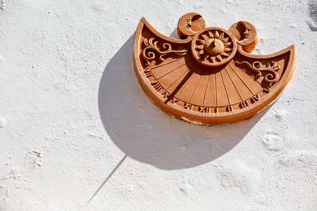 Terracotta sundial on a white wall of a house. Intense sun.