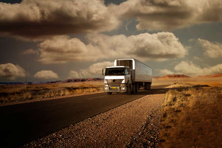 truck traveling on a paved road in the beautiful landscape of Namibia, and the desert scene with clouds in the sky, photographed at sunsetのeditorial素材