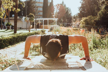 A boy does push-ups in a park of a little town. Warm light of sunset.の写真素材